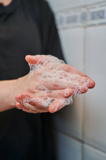 Lavarsi le mani con sapone per la prevenzione del coronavirus da una giovane ragazza con una t-shirt nera su un bagno piastrellato bianco
 - Foto, immagini