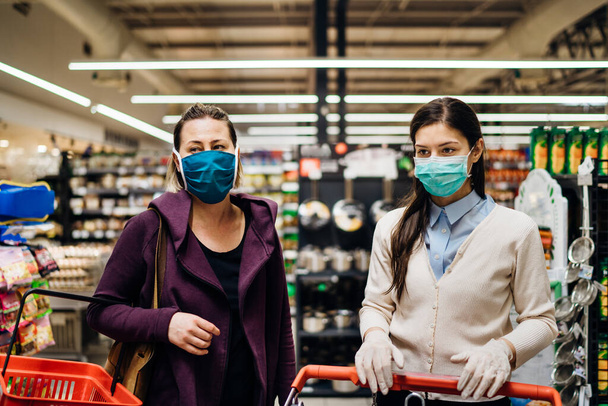 Shoppers with masks buying for groceries due to coronavirus pandemic in grocery store.COVID-19 food shopping.Quarantine preparation.Panic buying and stockpiling.Social distancing in supermarket - 写真・画像