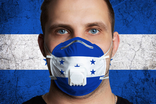 Young man with sore eyes in a medical mask painted in the colors of the national flag of Honduras. Coronovirus disease  COVID-19 concept.  Man is afraid of getting the flu - Photo, Image