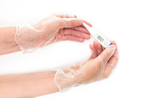 Γυναικεία χέρια που φορούν γάντια βινυλίου κρατώντας ένα ψηφιακό θερμόμετρο. Κοντινό πλάνο, απομονωμένο σε λευκό φόντο - Φωτογραφία, εικόνα
