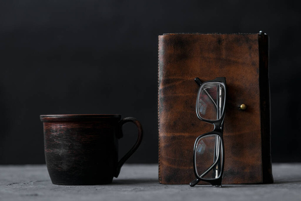 Brown leather notebook and glasses on wooden table. Businessman workspace with cup of black coffee. Business planning and work day organization. Coffee break at workplace in office. - Foto, Imagem