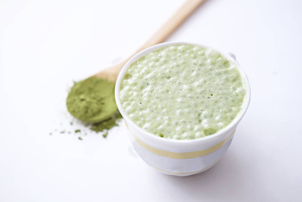 matcha latte in a cup and matcha powder in wooden spoon. healthy drinks concept. - Foto, Bild