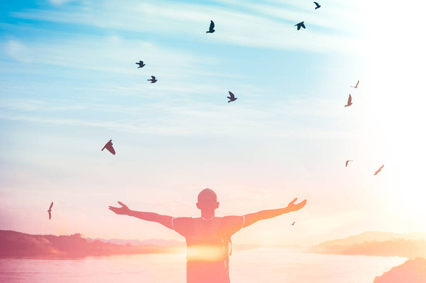 Onnellinen reppu mies nostaa kätensä ylös ja linnut lentävät auringonlaskun taivaalla joen taustalla. Matkaseikkailu ja vapaus tuntuvat hyvältä konseptilta. Vintage sävy suodatin vaikutus väri tyyli
 - Valokuva, kuva