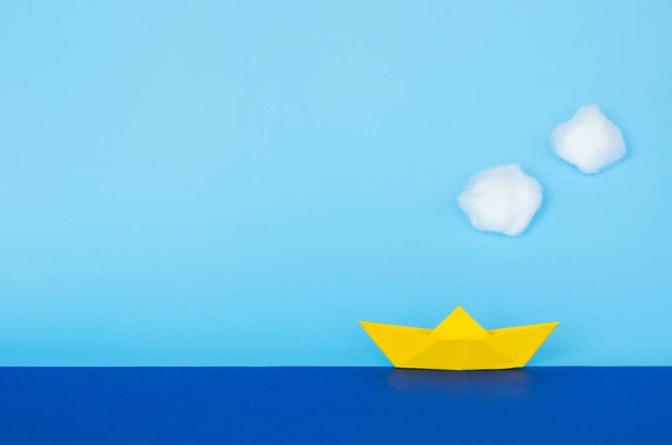 Keltainen paperi vene liikkuu sinisellä merellä taivaalla ja pilvet. Minimaalinen matka ja loma käsite
. - Valokuva, kuva