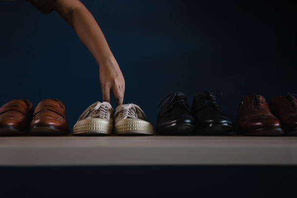 Ανδρικά παπούτσια μόδας. Άντρας διαλέγει αθλητικά παπούτσια για να φορέσει. Εγκατάλειψη εργασίας ή εξισορρόπηση έννοιας χαλάρωσης - Φωτογραφία, εικόνα