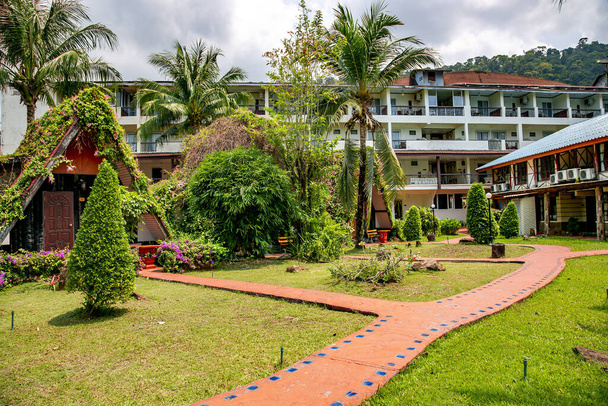Edificio blanco de un pequeño hotel rodeado por un hermoso parque tropical con pasarelas de ladrillo rojo en la isla tropical de Koh Chang en Tailandia
. - Foto, Imagen