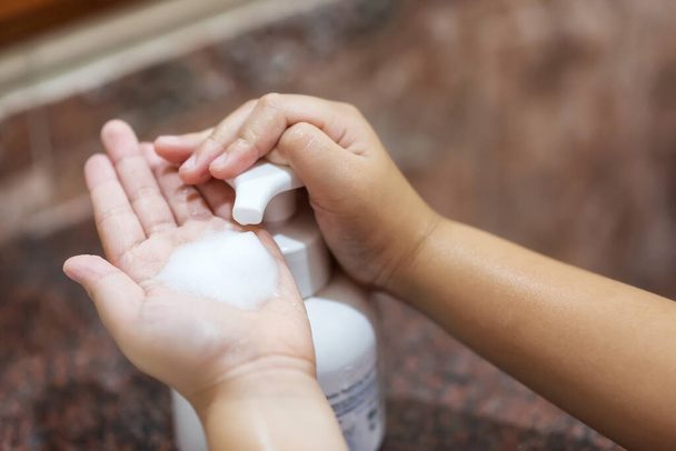 Детские руки получают антибактериальное мыло с пеной для дезинфицирующего средства в ванной или туалете. Дети моют руки, чтобы предотвратить ковид-19 или коронавирусную болезнь. Социальное дистанцирование, безопасность дома, карантин
. - Фото, изображение