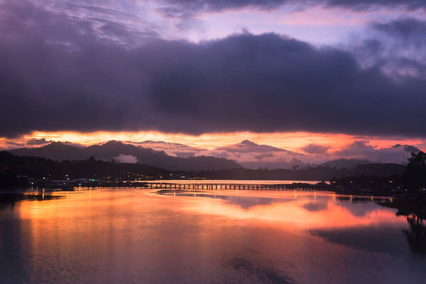 Silhouette Mon ville et pont en bois sur la rivière Songkalia avec nuage, ciel crépusculaire, réflexion de la lumière à l'aube à Sangkhlaburi, Kanchanaburi, Thaïlande. Destination de voyage célèbre en thaï
. - Photo, image
