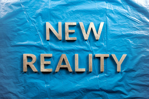 las palabras nueva realidad colocada con letras blancas sobre fondo de película de plástico azul arrugado en directamente por encima de la perspectiva
 - Foto, Imagen