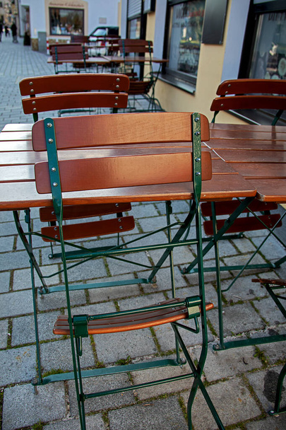 folded up beer garden chairs and empty tables in front of a street bar - Photo, Image