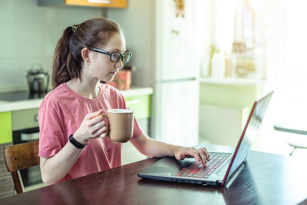 Uma jovem trabalha remotamente em um laptop em casa. O conceito de trabalho à distância e educação online. Passatempo útil quando você tem que ficar em casa
. - Foto, Imagem