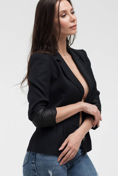 Gorąca brunetka kobieta z nagimi piersiami dotykając czarny garnitur i prowokacyjnie patrząc daleko w studio - Zdjęcie, obraz