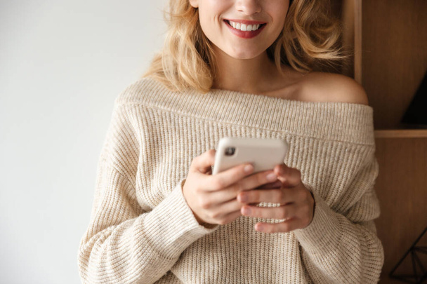 Cropped image of a smiling young woman indoors at home using mobile phone. - Photo, image