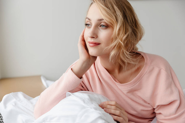 Image of a beautiful positive optimistic young woman posing indoors at home in bedroom under blanket. - Φωτογραφία, εικόνα