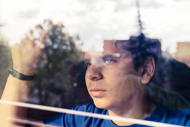 Παιδί κοιτάζει έξω από το παράθυρο στο δρόμο περιμένοντας το τέλος του εγκλεισμού λόγω της πανδημίας από COVID-19 - Φωτογραφία, εικόνα