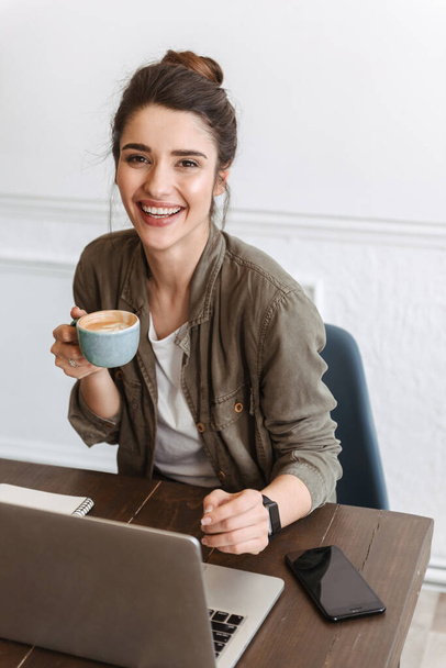Lovely young woman using laptop computer while sitting at the cafe indoors, drinking coffee - Foto, Bild