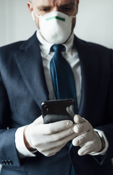 Empresario con máscara y guantes de látex usando teléfono inteligente
 - Foto, imagen