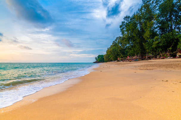 Uitzicht op het tropische strand van Koh Lanta eiland, Thailand. Bar op het strand zijn voorbereid voor toeristen tijdens de prachtige zonsondergang. Zacht licht, levendige kleuren. Lucht met wolken boven rustige zee. - Foto, afbeelding