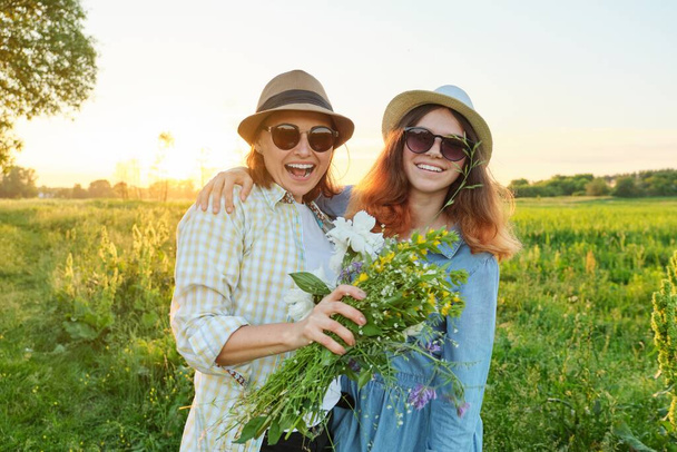 Mothers day, hugging happy smiling teenager daughter with mother in meadow with bouquet of spring flowers - 写真・画像