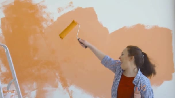 Έννοια του τρόπου ζωής Singleton. Νεαρή ευτυχισμένη γυναίκα βάφει τους τοίχους της πορτοκαλί με ένα ρολό - Πλάνα, βίντεο
