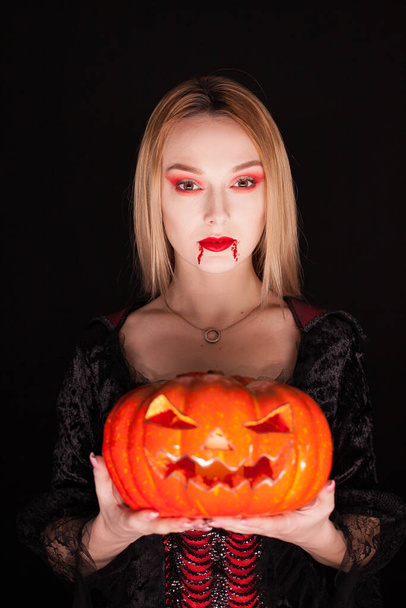 Beautiful girl dressed up like a vampire holding a pumpkin - Fotó, kép