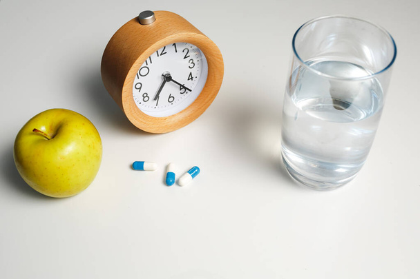 Alarm clock, glass of water and white pills on white table background - Photo, Image