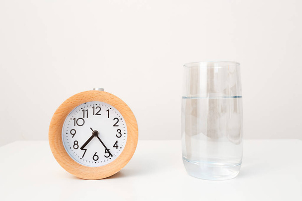 Alarm hodiny a sklenice vody na bílém stolku pozadí - Fotografie, Obrázek