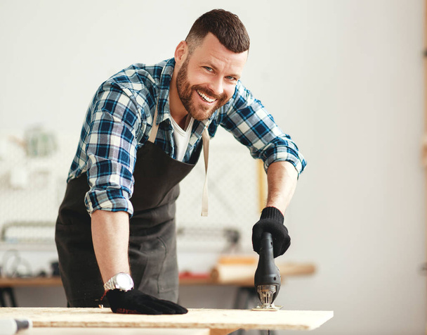 junger glücklicher männlicher Tischler, der in einer Werkstatt arbeitet - Foto, Bild