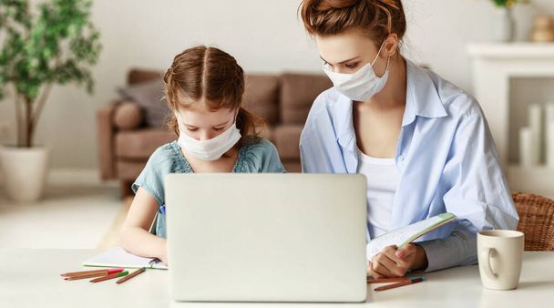 Uitgeputte vrouw in medisch masker zit aan tafel en kijkt ijverig meisje werken op laptop terwijl het doen van huiswerk samen tijdens de pandemie - Foto, afbeelding