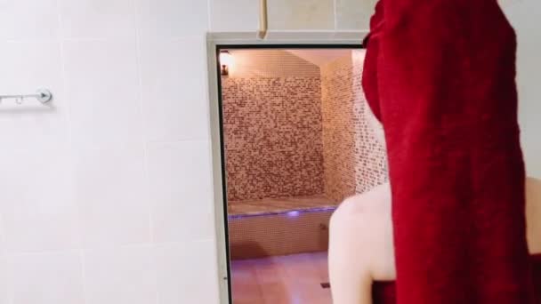 Een meisje komt in een hammam gekleed in rode handdoeken - Video