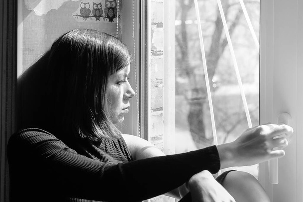 preto e branco imagem de um triste jovem bonita morena em roupas pretas olhando para fora da janela
 - Foto, Imagem