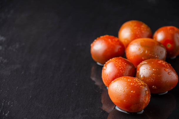 Horní pohled na skupinu mokrých kumato cherry rajčat, se selektivním zaměřením, na černou břidlici vodorovně, s kopírovacím prostorem - Fotografie, Obrázek