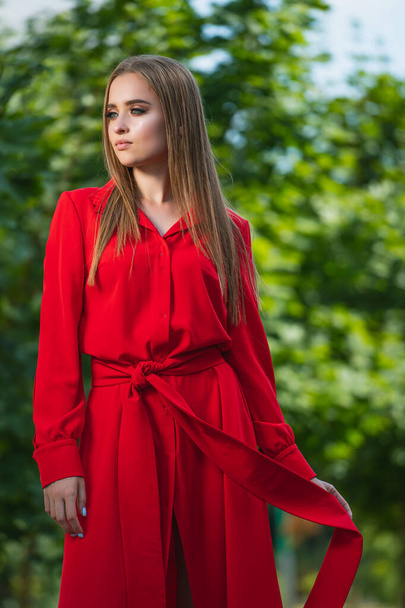 Photo of attractive woman wearing red dress on a green tree background. Long hair. Portrait of a beautiful girl. Young female photo session. - Foto, Imagem