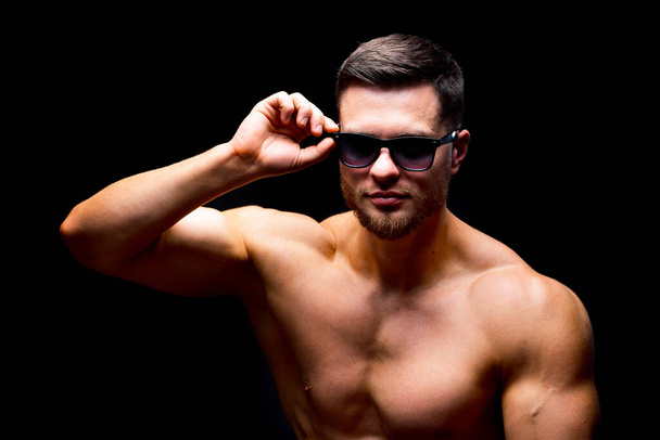 Well build handsome man without a shirt posing in studio. Strong body and cool face. Male wearing glasses. Portrait. Selective focus. Closeup. - 写真・画像