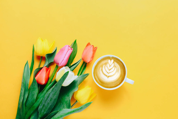 Kupa kávé és gyönyörű tulipán sárga háttér, felső nézet - Fotó, kép