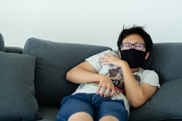 Asian Men Wearing Glasses Wearing a black mask Sleeping on the grill sofa in his room.A sick man is sleeping.On the griay sofa someone was resting.. - Foto, Imagen