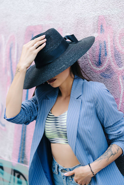 Mavi çizgili ceket ve siyah şapka giymiş genç bir kızın moda portresi. - Fotoğraf, Görsel