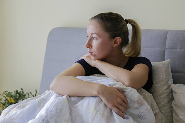 Depressed single woman sitting at home due to worldwide quarantine lockdown. Portrait of lonely stressed out female alone in her bed. Close up, copy space, background. - Photo, image