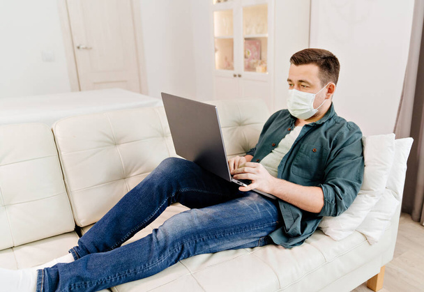 male blogger in medical mask working on couch - Fotoğraf, Görsel