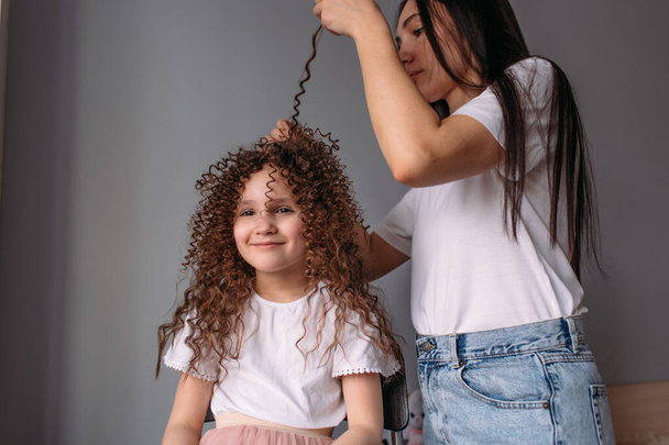 Mom made her daughter a hairstyle, a lot of curls, daughter is happy and plays with curls - Fotografie, Obrázek