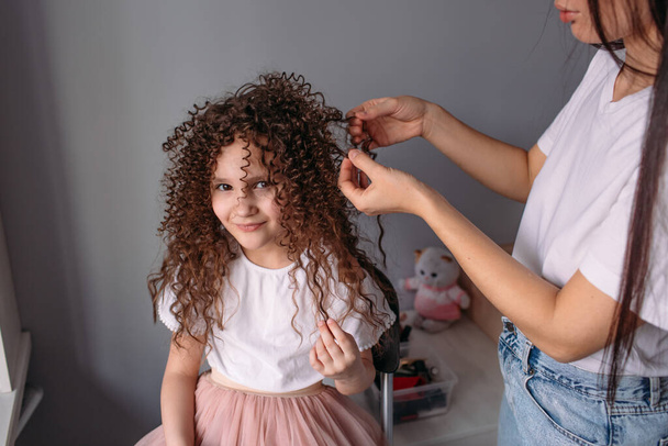 Mom made her daughter a hairstyle, a lot of curls, daughter is happy and plays with curls - Foto, Bild