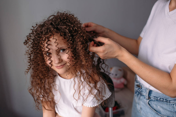 Mom made her daughter a hairstyle, a lot of curls, daughter is happy and plays with curls - Photo, Image