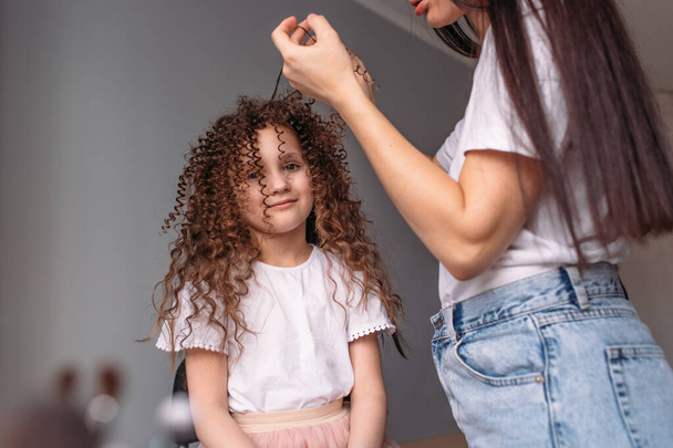 Mom made her daughter a hairstyle, a lot of curls, daughter is happy and plays with curls - Fotografie, Obrázek