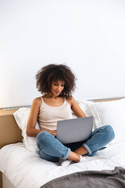 Image of beautiful concentrated young african woman indoors at home using laptop computer sit in bed. - Foto, immagini