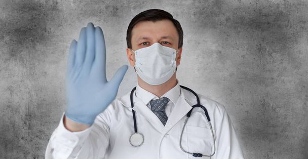 Medical staff preventive gear against coronavirus. Male doctor in face mask showing stop sign with his hand - Foto, afbeelding