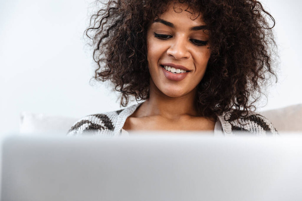 Image of beautiful positive smiling young african woman indoors at home using laptop computer. - Foto, Bild