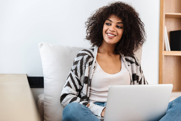 Image of cheerful happy young african woman indoors at home using laptop computer. - Foto, Imagem