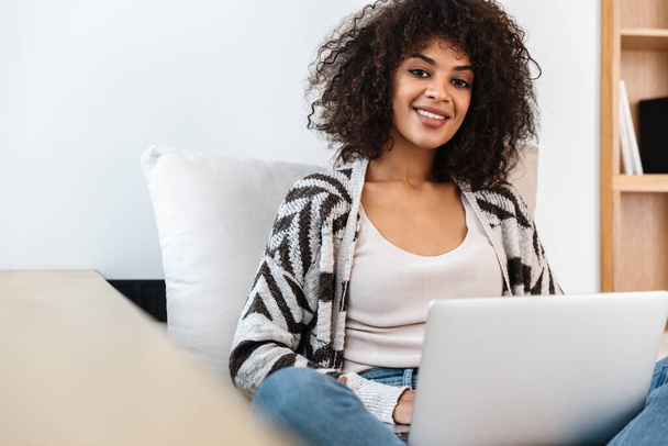 Image of cheerful happy young african woman indoors at home using laptop computer. - Foto, Bild