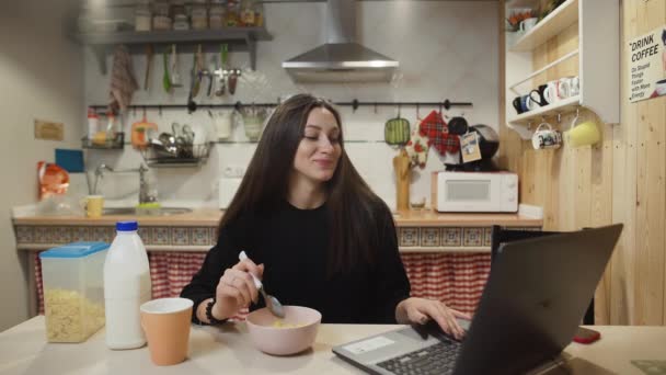 Young woman working laptop computer and eats Corn Flakes Cereal at home kitchen. - Séquence, vidéo