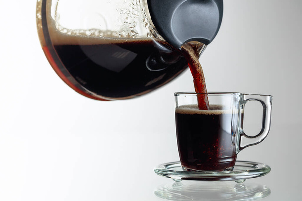 Café negro en una taza de vidrio sobre una mesa de vidrio. El café se vierte de la cafetera en una taza. Copiar espacio
. - Foto, imagen